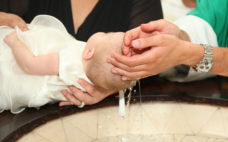 Newborn baby baptism by water with hands of priest