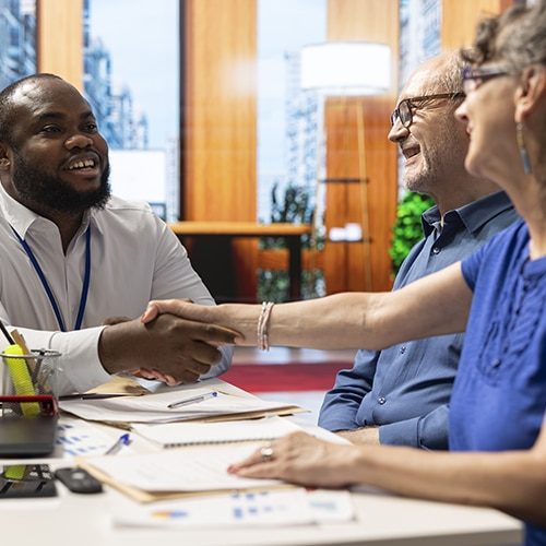 Financial expert sharing a handshake with old woman client during a counseling meeting in modern office. Adviser guiding senior people to choose a retirement plan with life insurance.
